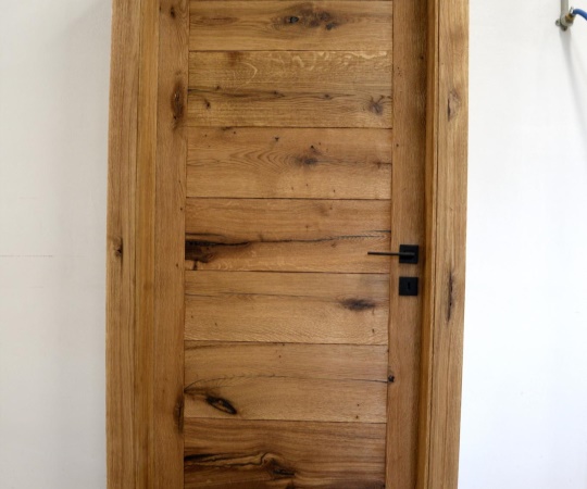 Dveře jednokřídlé, vodorovně fošnové v obložkové zárubni. Rustikální dubové dřevo, hluboce drásané, olejované. Černá klika a závěsy. Klika Terry
