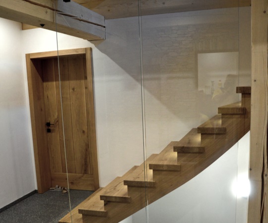 Sedlový obklad betonových schodů se skleněným zábradlím a podsvícením LED pásky a fošnové vnitřní dveře v obložkové zárubni z dubového dřeva.