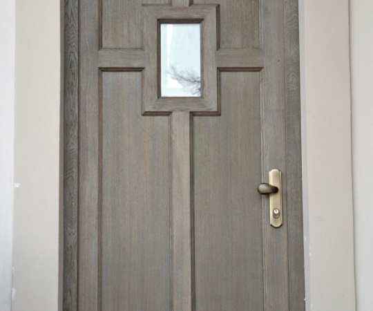 Dveře vstupní, jednokřídlé, kazetové v rámové zárubni dubové dřevo, drásané, nátěr lazurou. Prosklené okénko.