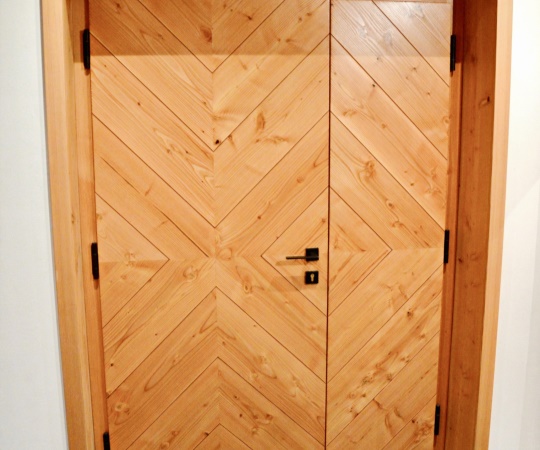 Vstupní dveře dvoukřídlé, prkenné s motivem kosočtverce (routa), v rámové zárubni s obložkou, douglaskové dřevo, nátěr lazurou.