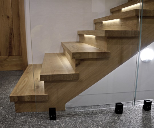 Detail sedlového obkladu betonových schodů se skleněným zábradlím a podsvícením LED pásky z dubového dřeva.