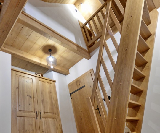 Dominantou interiéru jsou dubové schody s galerií, které zaujmou čistým řemeslným zpracováním a přirozenou kresbou dřeva. Celek doplňují dubové interiérové dveře s kovaným kováním a vestavná šatní skříň na míru, sjednocené jednotným designem a ošetřené přírodním olejem. Výsledkem je nadčasový a odolný interiér ideální pro roubenky i stylové venkovské bydlení.