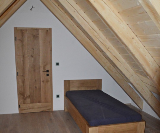 Moderní postel a fošnové vnitřní dveře v obložkové zárubni, vše z dubového dřeva.