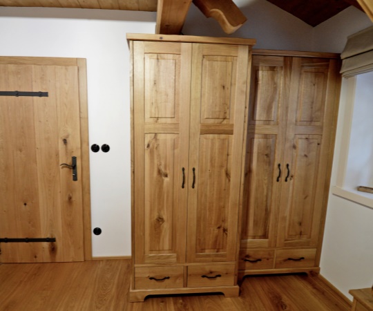 Sestava šatních skříní stylově navazující na fošnové svlakované dveře, navržená tak, aby plnohodnotně využila jinak obtížně využitelný prostor vedle okna. Dveře i skříně jsou vyrobeny z masivního dubu, s povrchovou úpravou drásáním a olejovým nátěrem. Skříně i dveře jsou osazeny kovanými závěsy, klikou a úchytkami.