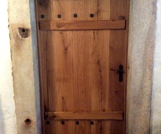 Jednokřídlé fošnové svlakované dveře, dubový masiv drásaný, tesaný, nátěr olejem, kované závěsy a zámek myšák.
