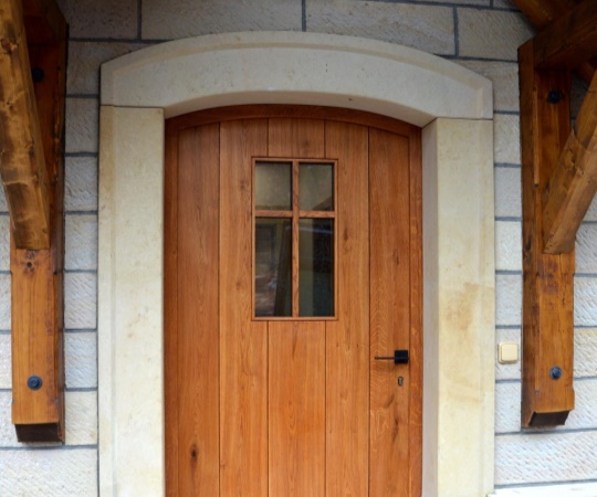 Dveře vstupní fošnové, obloukové s okénkem, jednokřídlé, rámová zárubni v kamenném ostění, dub, drásané, nátěr lazurou.