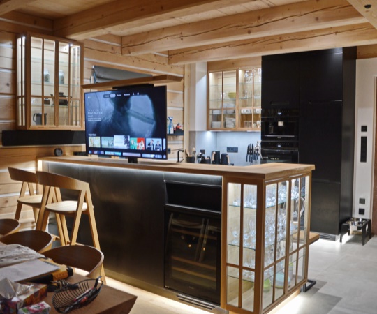 Moderní kuchyně na míru kombinuje masivní dřevo s černými plochami, čisté linie a promyšlené detaily. Dominantou prostoru je kuchyňské rameno s barem, které slouží nejen pro přípravu jídla, ale i pro posezení. Jeho součástí je výsuvná televize, nenápadně ukrytá uvnitř nábytku, která se vysune pouze v případě potřeby.

Díky tomu zůstává kuchyně vizuálně čistá a nerušená. Celkové řešení klade důraz na funkčnost a maximální využití prostoru v moderním interiéru.