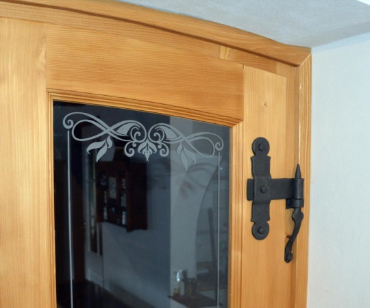 Detail dveří, pískovaný motiv na skle a kovaný dveřní závěs.