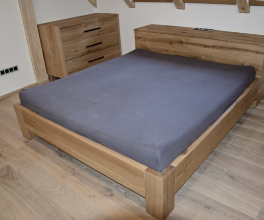 Manželská postel s peřiňákem a komoda, vše v moderním hladkém stylu z dubového dřeva.