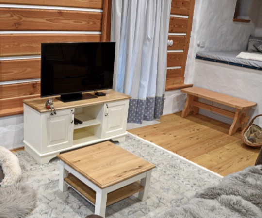 Televizní a konferenční stolek v kombinaci smrkového dřeva s bílým krycím nátěrem a dubového, jemně drásaného dřeva ošetřeného přírodním olejem. Do interiéru byla rovněž vyrobena selská lavice z douglasky, která přirozeně ladí s douglaskovým roubením.