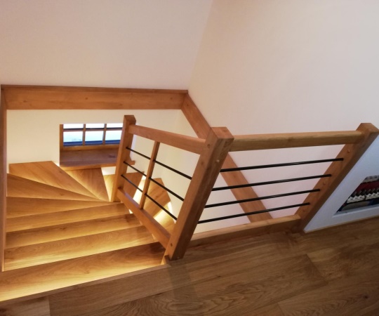 Obklad betonových schodů, včetně zábradlí, podstupňů a galerie, vyrobený z dubového dřeva, drásané, nátěr olejem. Výplň zábradlí, kovové černé tyče.